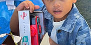 Jayden participe au concours pour gagner de l'argent avec cette photo : child, toddler, toy, toy_box, unwrapping, gift, wrapping_paper, denim_jacket, outdoor, grass, chair, curious, top_knot, happy, face, hand, present, colorful, daylight, person