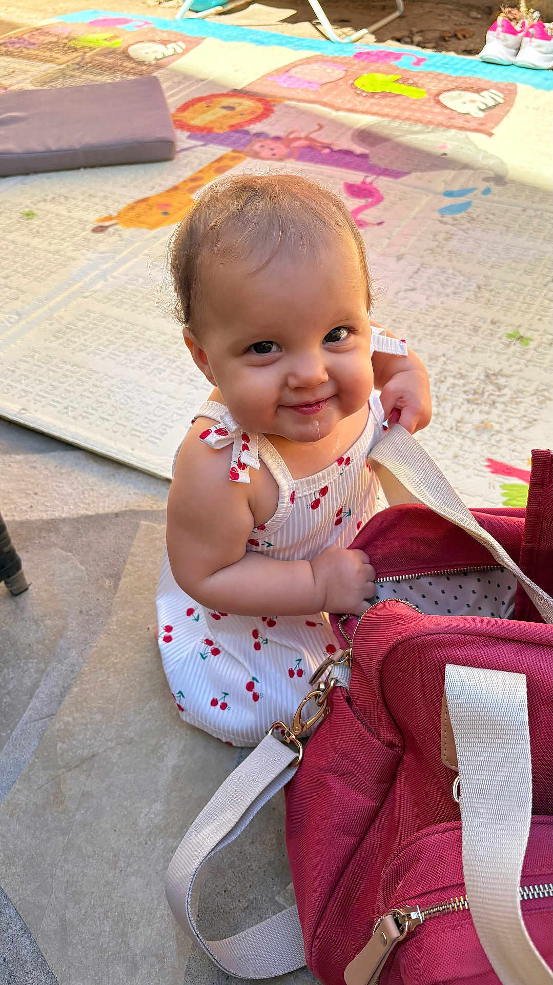 Charlotte a rejoint le concours — aidez-le/la à gagner de superbes lots ! baby, bag, cherry_pattern, child, concrete_floor, curious, cute, dress, drool, exploring, happy, infant, outdoor, person, play_mat, red_bag, sitting, smiling, sunlight, white_shoes