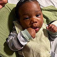 Kamari is registered to the contest to win money with this photo: baby, infant, child, face, hand, bib, striped_clothing, cushion, green, bottle, bed, resting, portrait, skin, eyes, mouth, fingers, closeup, indoor, person