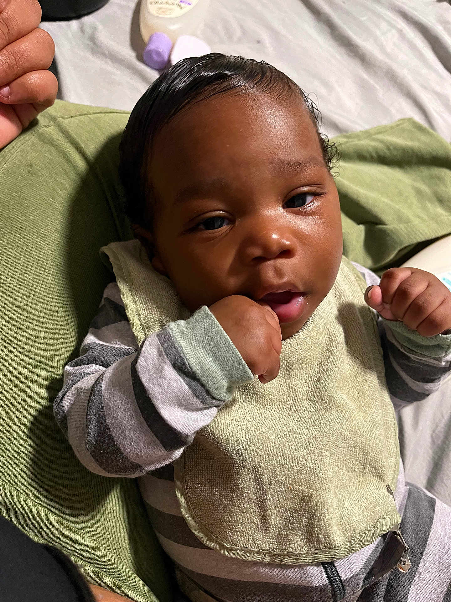 Kamari is registered to the contest to win money with this photo: baby, infant, child, face, hand, bib, striped_clothing, cushion, green, bottle, bed, resting, portrait, skin, eyes, mouth, fingers, closeup, indoor, person