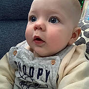 Theodore is registered to the contest to win money with this photo: baby, child, face, blue_eyes, rosy_cheeks, sitting, cozy_clothing, snoopy, indoor, couch, pillow, bookshelf, closeup, portrait, cute, soft_light, infant, clothing, button, expression