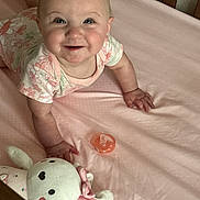 Sophia is registered to the contest to win money with this photo: baby, bed, child, crib, cute, face, foot, hand, happy, indoor, infant, light, onesie, pacifier, person, pink_sheet, plush_toy, smiling, soft, toy