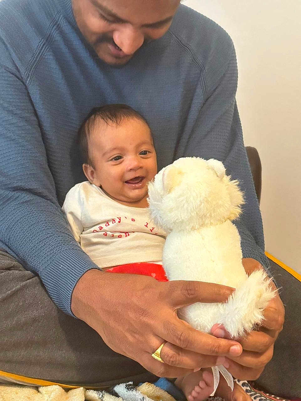 Thiyansh Jaswik is registered to the contest to win money with this photo: baby, adult, smile, stuffed_animal, toy, hands, clothing, sitting, indoor, blanket, happy, face, person, cuddle, warmth, family, bonding, casual, comfort, love