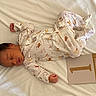 newborn, baby, sleeping, infant, onesie, bed, white_bed, milestone_card, animal_print, peaceful, cute, resting, soft, portrait, indoor, person, child, small, newborn_baby, baby_sleeping