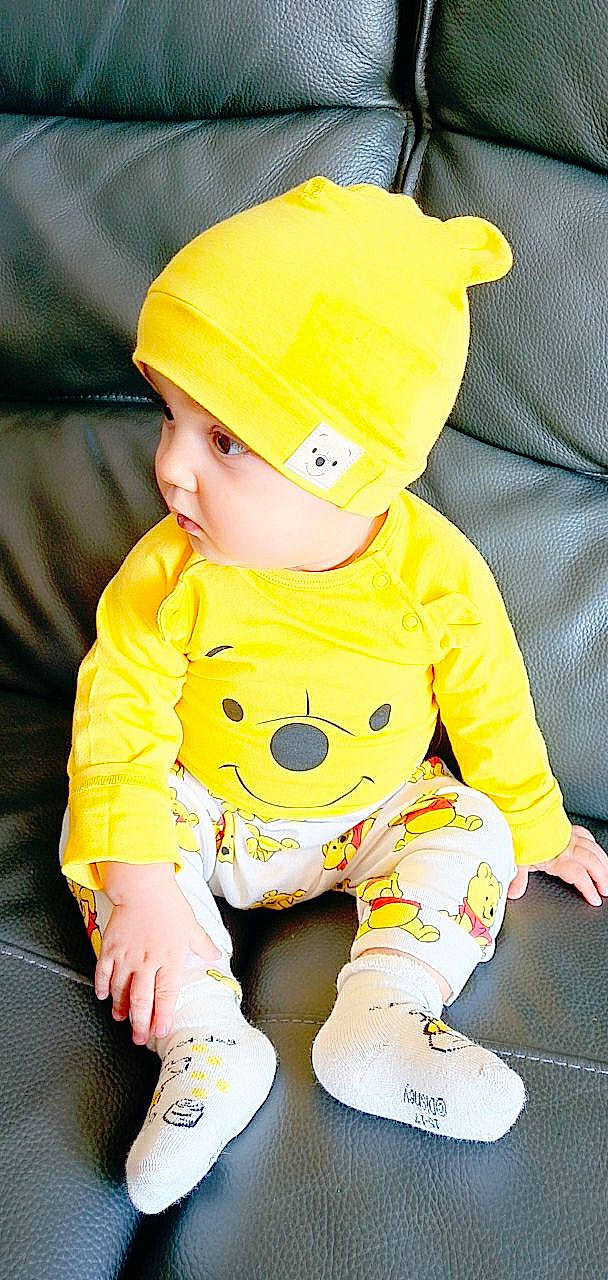 Logan participe au concours pour gagner de l'argent avec cette photo : baby, baby_products, baby_toddler_clothing, beanie, bonnet, child, comfort, cool, costume_accessory, couch, headwear, overall, person, sitting, sleeve, toddler, yellow