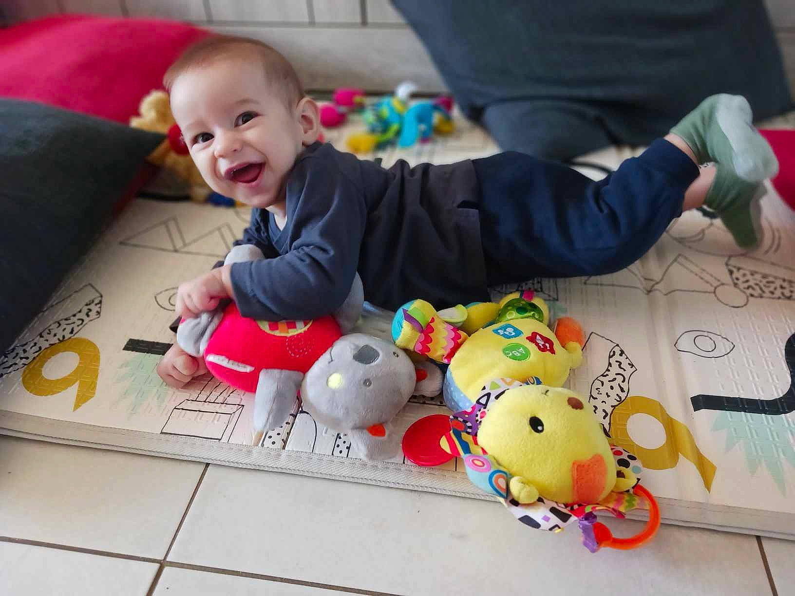 Neel a rejoint le concours — aidez-le/la à gagner de superbes lots ! baby, baby_products, baby_toddler_clothing, baby_toys, child, comfort, couch, event, floor, flooring, fun, happy, mammal, person, smile, stuffed_toy, textile, toddler, toy, white