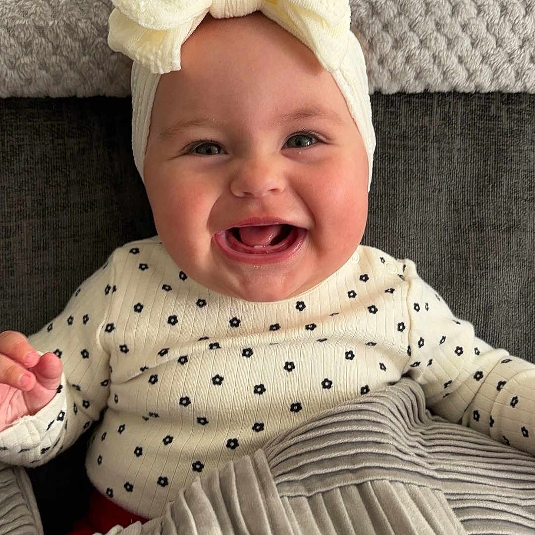 Neve joined the competition — help win amazing prizes! baby, babylaughing, bodypart, clothing, couch, cushion, dress, face, furniture, happy, hat, head, homedecor, laughing, mouth, newborn, person, photography, portrait, smile