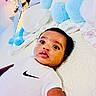 baby, bed, bedding, bedroom, blue, child, clothing, cozy, face, indoor, infant, lying_down, nike_shirt, pastel, photograph, plush_toy, portrait, stuffed_animal, white, wide_eyes