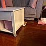 cat, orange_cat, peeking, coffee_table, gray_couch, pink_cushions, wooden_floor, indoor, curious, pet, furniture, living_room, floor, cozy, home, domestic_cat, playful, animal, resting, cute