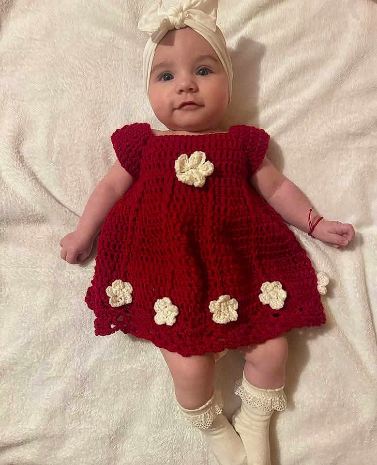 Eva Cataleya a rejoint le concours — aidez-le/la à gagner de superbes lots ! baby, infant, child, crocheted_dress, red_dress, headband, socks, white_blanket, flower_decorations, handmade_clothing, cute, portrait, laying_down, smiling, soft_texture, indoors, light_skin, happy, fashion, baby_fashion