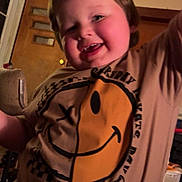 Joshua joined the competition — help win amazing prizes! child, toddler, smiling, indoor, tshirt, graphic_tshirt, smiley_face, skateboard, happy, person, face, arm_raised, brown_hair, room, door, window, furniture, cozy, warm_lighting, casual_clothing