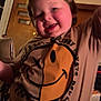 child, toddler, smiling, indoor, tshirt, graphic_tshirt, smiley_face, skateboard, happy, person, face, arm_raised, brown_hair, room, door, window, furniture, cozy, warm_lighting, casual_clothing