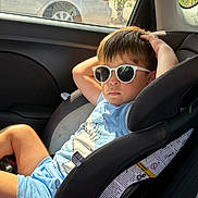 Kaleth is registered to the contest to win money with this photo: child, boy, sunglasses, car_seat, car_interior, sunlight, relaxed, casual_clothing, blue_shorts, blue_tshirt, seatbelt, window, car, vehicle, summer, shade, portrait, young, cool, leisure