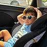 child, boy, sunglasses, car_seat, car_interior, sunlight, relaxed, casual_clothing, blue_shorts, blue_tshirt, seatbelt, window, car, vehicle, summer, shade, portrait, young, cool, leisure