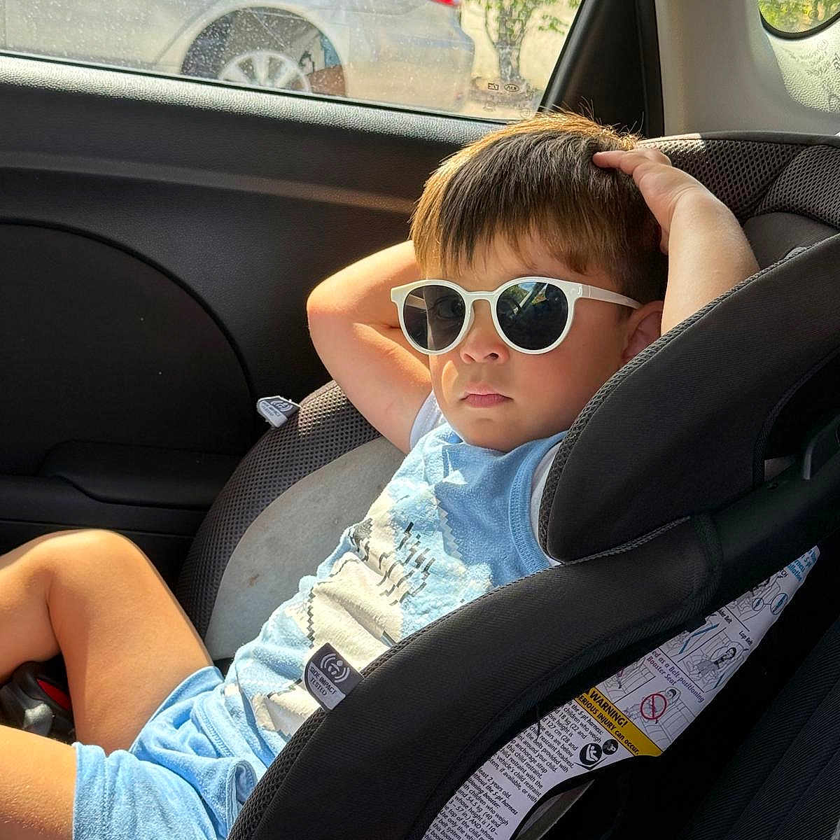 Kaleth is registered to the contest to win money with this photo: child, boy, sunglasses, car_seat, car_interior, sunlight, relaxed, casual_clothing, blue_shorts, blue_tshirt, seatbelt, window, car, vehicle, summer, shade, portrait, young, cool, leisure