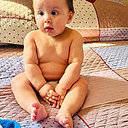 Wesly is registered to the contest to win money with this photo: baby, child, infant, bed, blanket, quilt, skin, barefoot, hands, feet, indoors, cute, curious, sitting, portrait, natural_light, home, soft, comfort, expression
