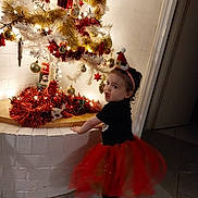 Inaya participe au concours pour gagner de l'argent avec cette photo : brick_wall, celebration, child, christmas_tree, cute, decor, festive, floor_tiles, holiday, holiday_decorations, indoor, lights, ornaments, person, red_tutu, santa_hat, smiling, tinsel, toddler, white_tree