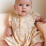 Ozzy joined the competition — help win amazing prizes! baby, child, infant, dress, headband, pink_bow, cute, soft_blanket, sitting, portrait, indoors, skin, face, hands, feet, expression, curious, floral_pattern, comfortable, adorable