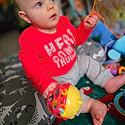 Liam is registered to the contest to win money with this photo: baby, infant, child, toddler, red_shirt, toy, rattle, playing, sitting, blanket, playmat, curious_gaze, hand, foot, portrait, indoor, bokeh, nursery, soft_toys, colorful