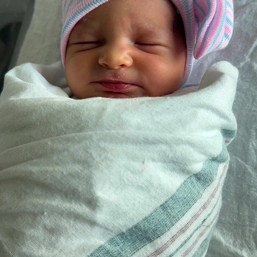 Saige is registered to the contest to win money with this photo: newborn, baby, sleeping, hat, striped_hat, bow, wrapped, blanket, hospital, infant, cute, peaceful, portrait, person, child, resting, soft, cozy, swaddled, indoors