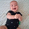 baby, infant, smiling, happy, onesie, space_theme, crib, patterned_sheet, clasped_hands, lying_down, cute, child, person, skin, head, face, expression, indoors, baby_clothing, playful