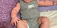 Kashe is registered to the contest to win money with this photo: baby, infant, child, onesie, nike, gray_clothing, white_socks, bed, blanket, purple_blanket, cream_blanket, chubby_arms, chubby_legs, blue_eyes, curious_expression, indoor, portrait, person, cute, relaxed