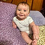 baby, infant, smiling, blue_eyes, onesie, pillow, purple, pattern, blanket, leopard_print, hand, foot, wooden_headboard, indoor, child, cute, happy, person, sitting, cozy