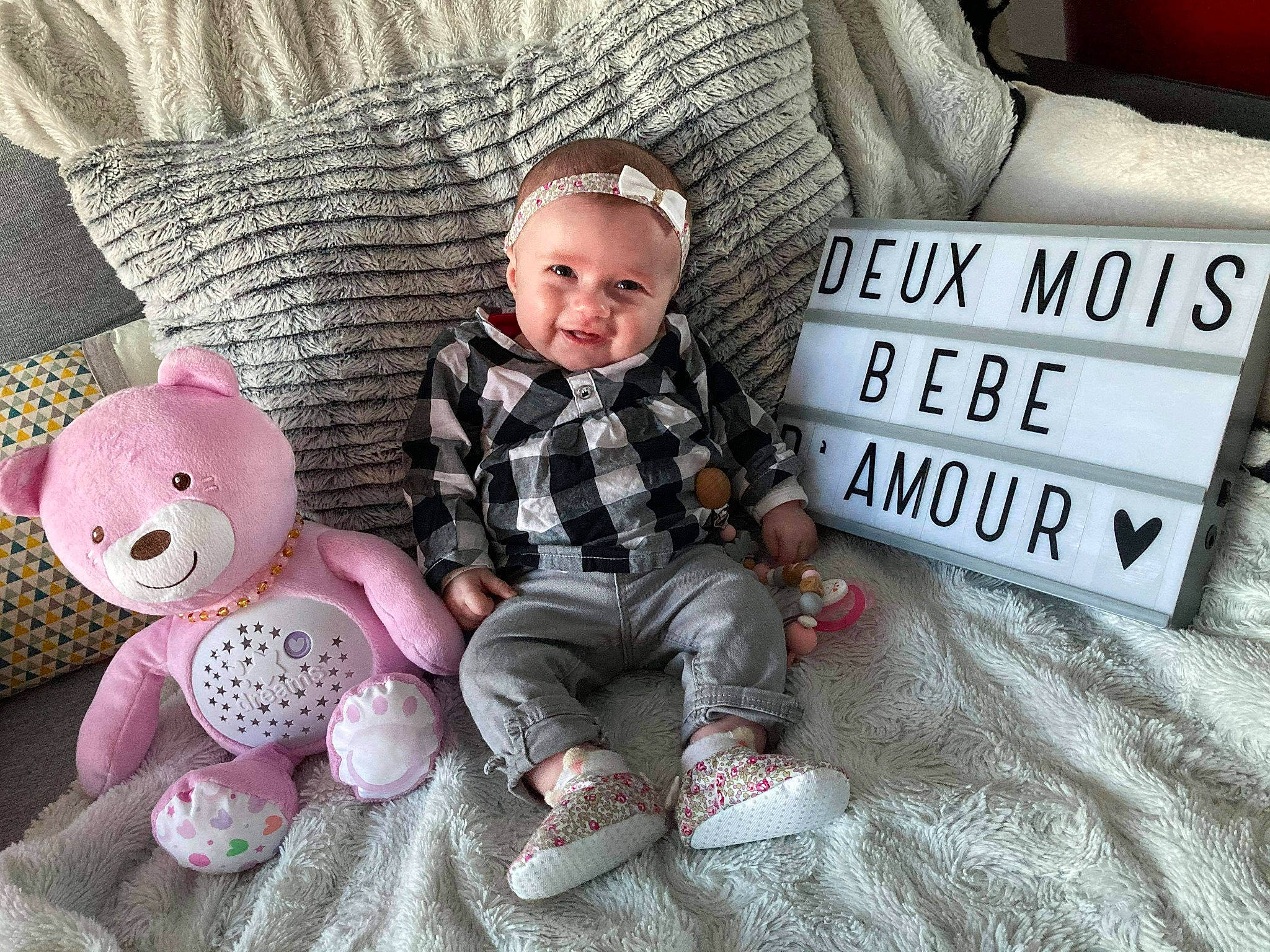 Lina participe au concours pour gagner de l'argent avec cette photo : baby, baby_toddler_clothing, child, comfort, couch, doll, face, headgear, lap, linens, pattern, person, pillow, room, sitting, sleeve, smile, toddler, toy, wood