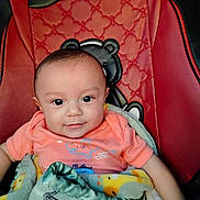 Jose is registered to the contest to win money with this photo: baby, infant, smile, blanket, red_chair, black_chair, teddy_bear, cute, child, clothing, portrait, indoors, furniture, cozy, happy, young_child, wrapped, seat, sitting, face
