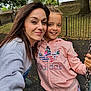 woman, child, swing, playground, outdoor, smile, happy, park, fence, tree, chain, hoodie, casual_clothing, portrait, friendship, nature, daylight, fun, family, leisure
