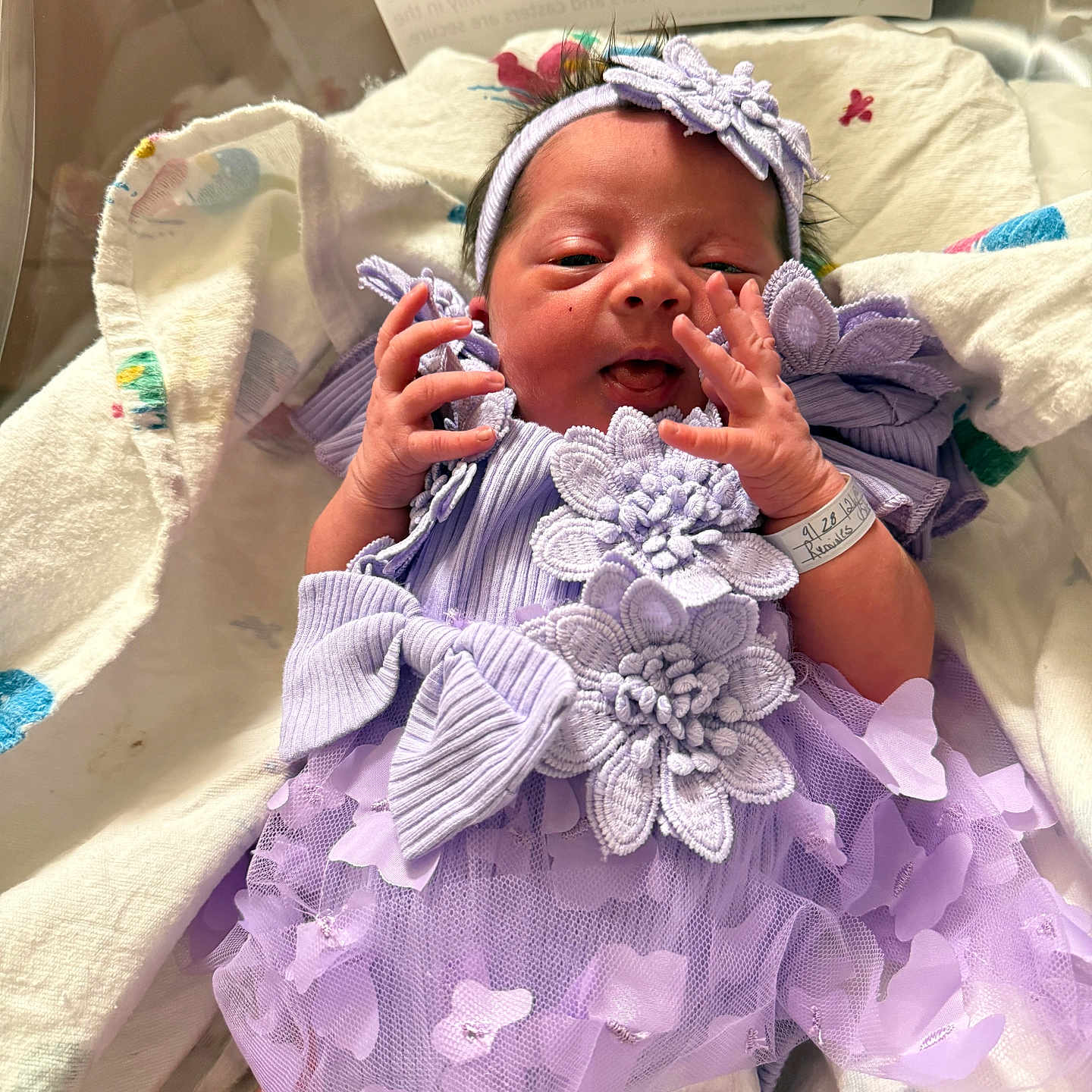 Elana joined the competition — help win amazing prizes! newborn, baby, infant, portrait, hospital, hospital_bed, blanket, lavender_dress, headband, bow, floral_dress, baby_girl, face, hands, smiling, awake, birth_card, bedding, indoor, photography