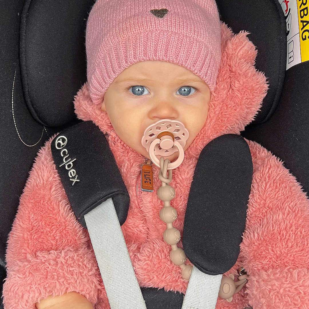 Lou participe au concours pour gagner de l'argent avec cette photo : baby, blue_eyes, car_seat, child, child_safety, close_up, cute, fluffy_jacket, indoors, infant, pacifier, person, pink_hat, pom_pom, portrait, safety_harness, seatbelt, warm, winter_clothing, young_child