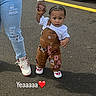 adult, asphalt, car, casual_clothing, child, daylight, emotion, expression, face, footwear, hair, hand_holding, outdoor, overalls, parking_lot, person, ripped_jeans, text_overlay, toddler, white_sneakers