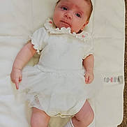 Daisy joined the competition — help win amazing prizes! baby, infant, white_clothing, white_mat, socks, cute, lying_down, portrait, child, newborn, soft_texture, indoors, curious_expression, small_hands, small_feet, tulle_skirt, pink_flower_detail, light_skin, red_hair, peaceful