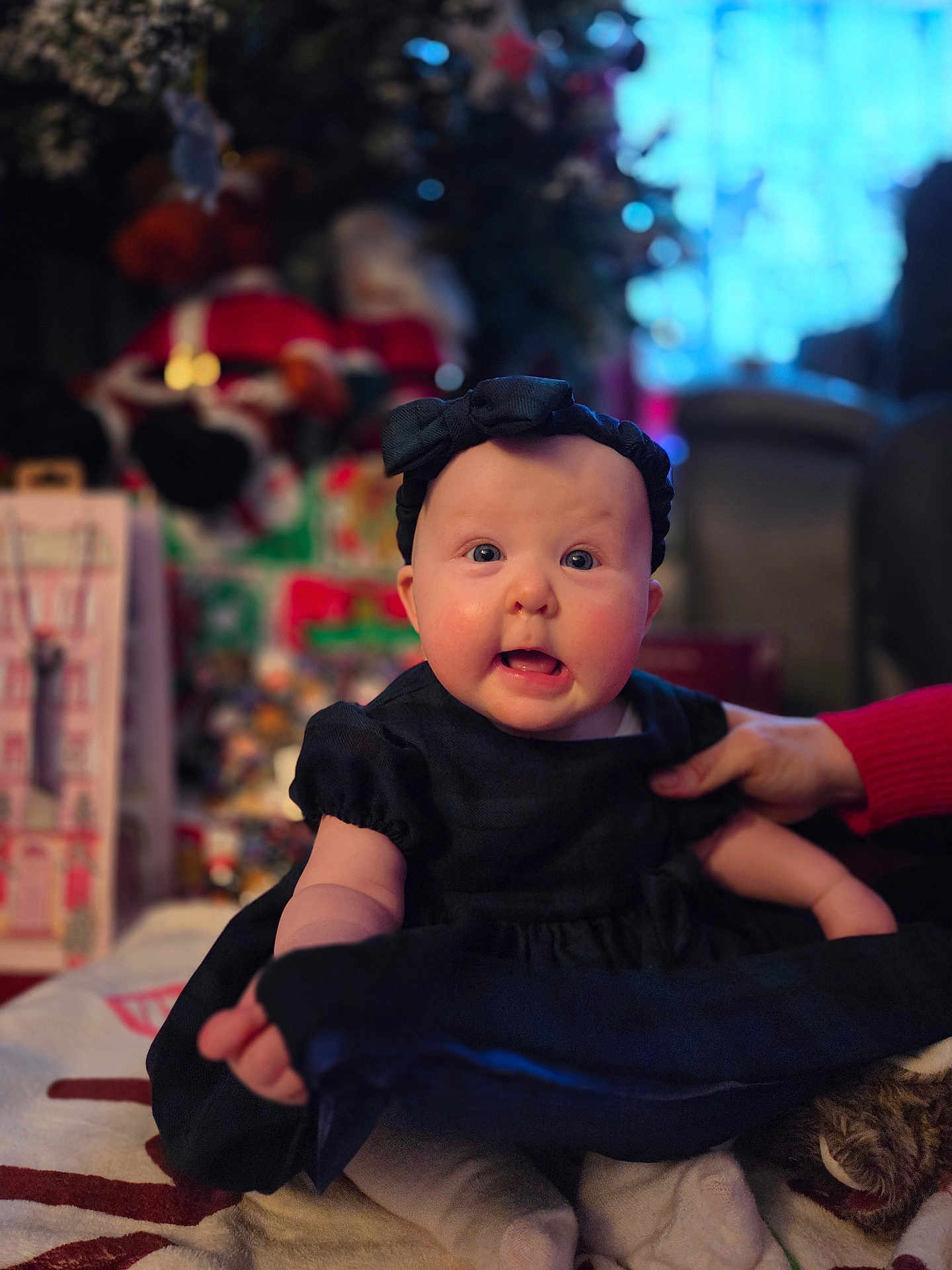 Marnie joined the competition — help win amazing prizes! baby, infant, child, black_dress, headband, hand, face, blue_eyes, expression, indoor, holiday, decorations, blurred_background, candid, cute, person, sitting, soft_lighting, festive, supporting_hand