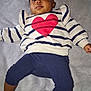 baby, child, person, face, sweater, heart, striped_clothing, pants, blanket, foot, hand, lying_down, indoors, soft_texture, casual_clothing, infant, cute, expression, portrait, young_child