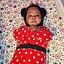baby, infant, onesie, polka_dot, red_clothing, hood, ears, bow, blanket, floral_pattern, crib, playpen, face, child, lying_down, indoors, cute, young_child, smiling, person