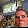 Rachel joined the competition — help win amazing prizes! cat, person, selfie, portrait, fluffy_cat, long_hair, tabby_cat, green_eyes, blue_eyes, indoors, home, couch, window, curtains, holiday_decorations, natural_light, close_up, face, cozy, pet_owner