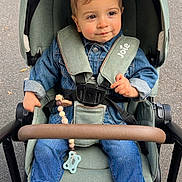 Elio participe au concours pour gagner de l'argent avec cette photo : child, baby, toddler, stroller, hood, seatbelt, denim_jacket, jeans, white_sneakers, pacifier, beads, toy, hand, face, smile, outdoor, pavement, wheel, joie_logo, fashion