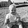 baby, child, smiling, outdoor, pebbles, black_and_white, happy, toddler, short_hair, sitting, cute, portrait, sunlight, playground, clothing, skirt, infant, person, head_accessory, nature
