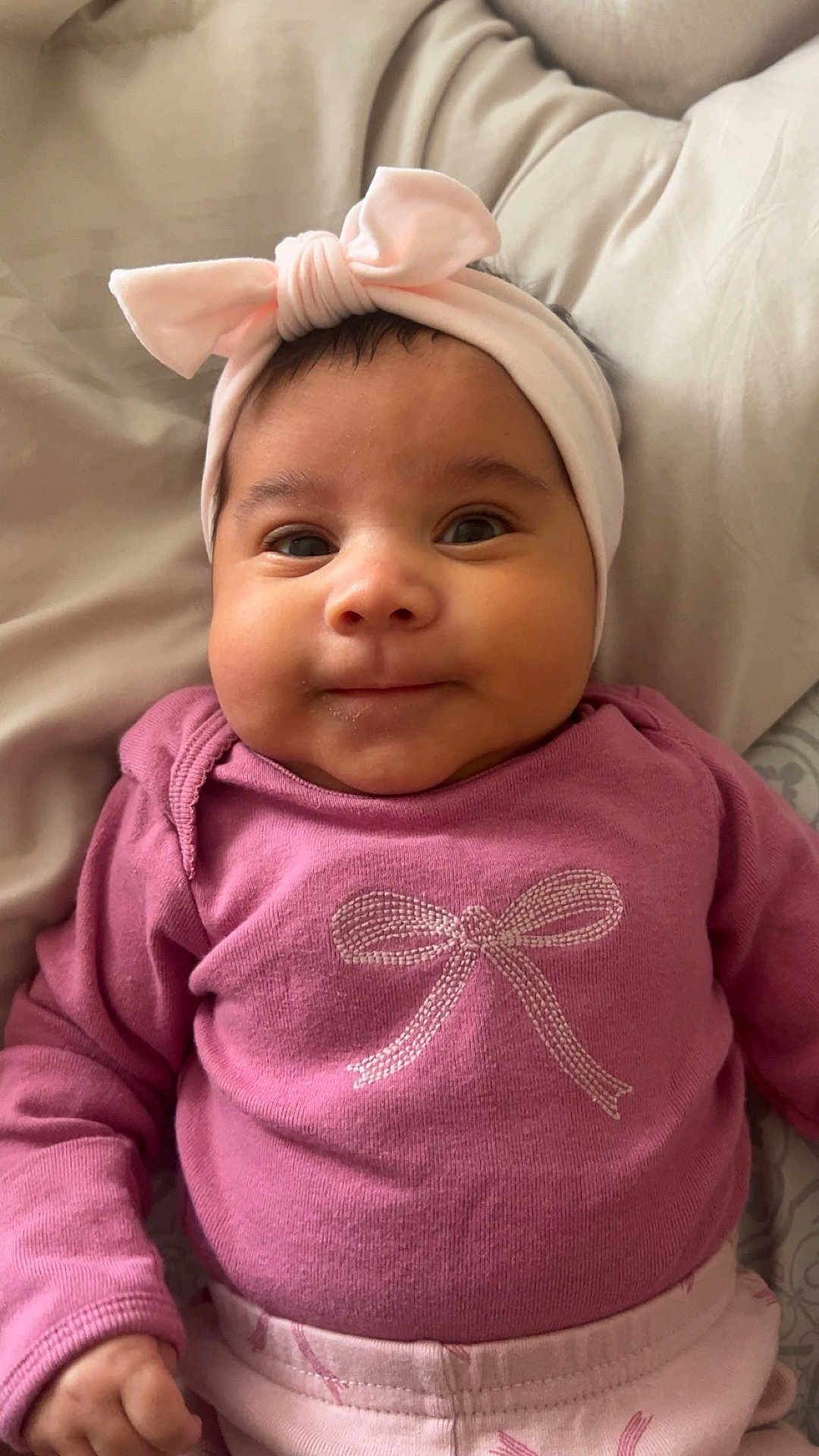 Eden joined the competition — help win amazing prizes! baby, infant, smiling, face, headband, pink_clothing, cute, child, portrait, indoors, lying_down, soft_lighting, cozy, hand, expression, apparel, fabric, bed, blanket, young_child