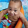 Cyairé is registered to the contest to win money with this photo: baby, blanket, blue, child, closeup, colorful, cute, diaper, face, fuzzy_rug, happy, indoors, infant, inflatable_pool, multicolored, orange, person, playful, skin, smile
