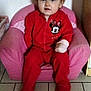 casual, child, clothing, curly_hair, cute, expression, face, furniture, hand_wrapped, home, indoor, minnie_mouse, pink_chair, portrait, red_onesie, sitting, small_chair, tile_floor, toddler, young_child