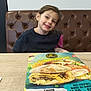 Amalia a rejoint le concours — aidez-le/la à gagner de superbes lots ! brown, burger, casual, child, clothing, dining, food, fries, girl, hair, happy, indoor, leather_booth, menu, portrait, restaurant, seated, smile, table, young