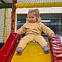 active, beige_clothing, blue_socks, child, curious, fun, happy, indoor, leisure, netting, padded, play, playground, recreation, red, safe, slide, toddler, yellow, young_child