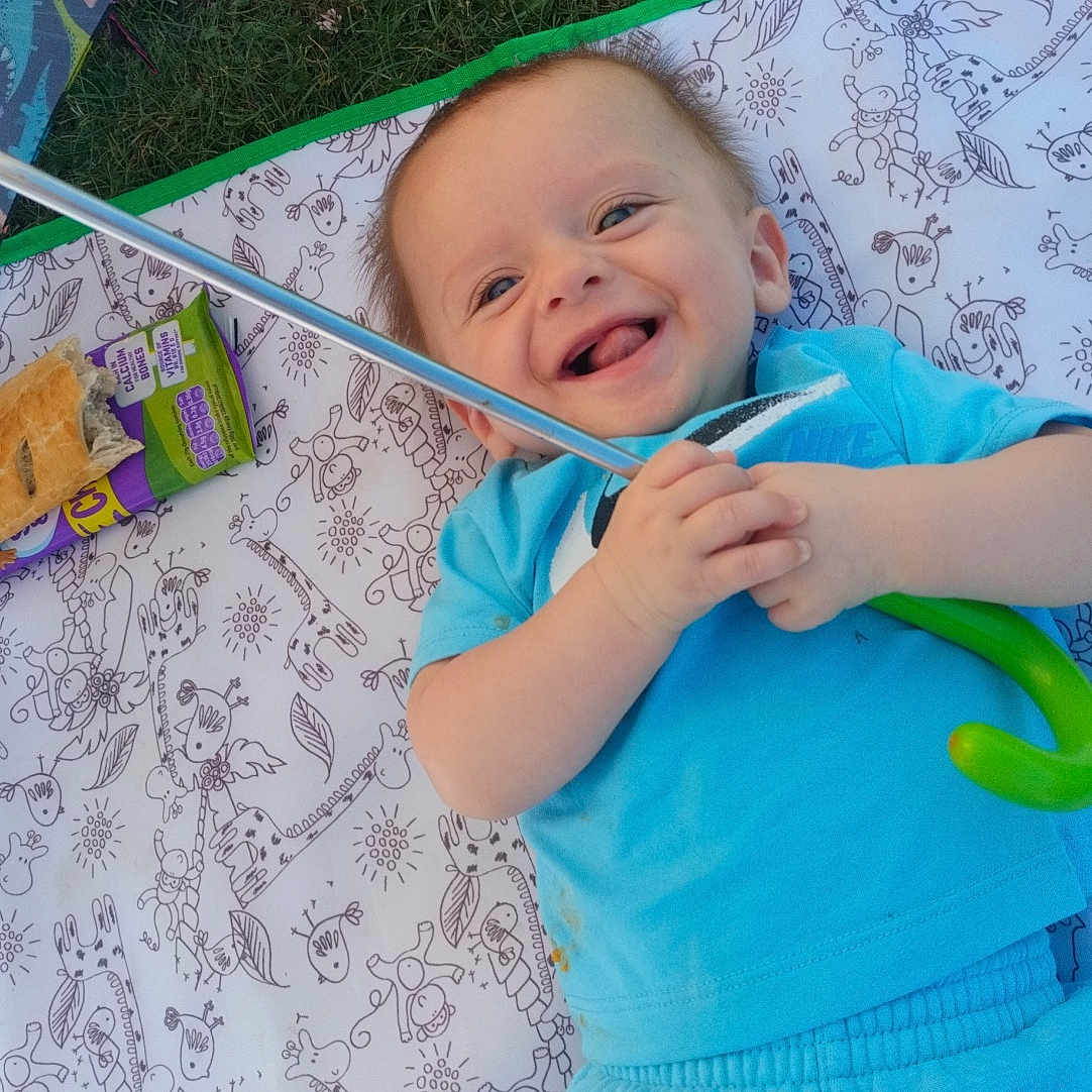 Hughie joined the competition — help win amazing prizes! baby, blanket, blue_clothing, child, cute, food, grass, happy, infant, laughter, outdoor, pattern, person, picnic, playful, relaxing, smiling, snack, toy, umbrella