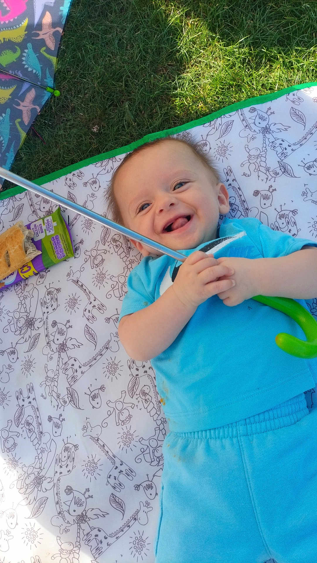 Hughie joined the competition — help win amazing prizes! baby, smiling, blue_clothing, blanket, grass, umbrella, snack, food, outdoor, happy, child, playful, infant, toy, pattern, picnic, laughter, person, cute, relaxing