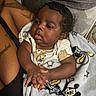 Messiah is registered to the contest to win money with this photo: baby, infant, child, portrait, sitting, indoors, chair, blanket, mickey_mouse, cartoon, adult, arm, tattoo, dark_skin, curly_hair, onesie, hands, cozy, candid, home