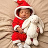 baby, infant, sleeping, santa_costume, christmas, red_outfit, winter, bunny, stuffed_animal, plush_toy, blanket, bed, portrait, indoors, cozy, peaceful, hands, socks, festive, soft_lighting