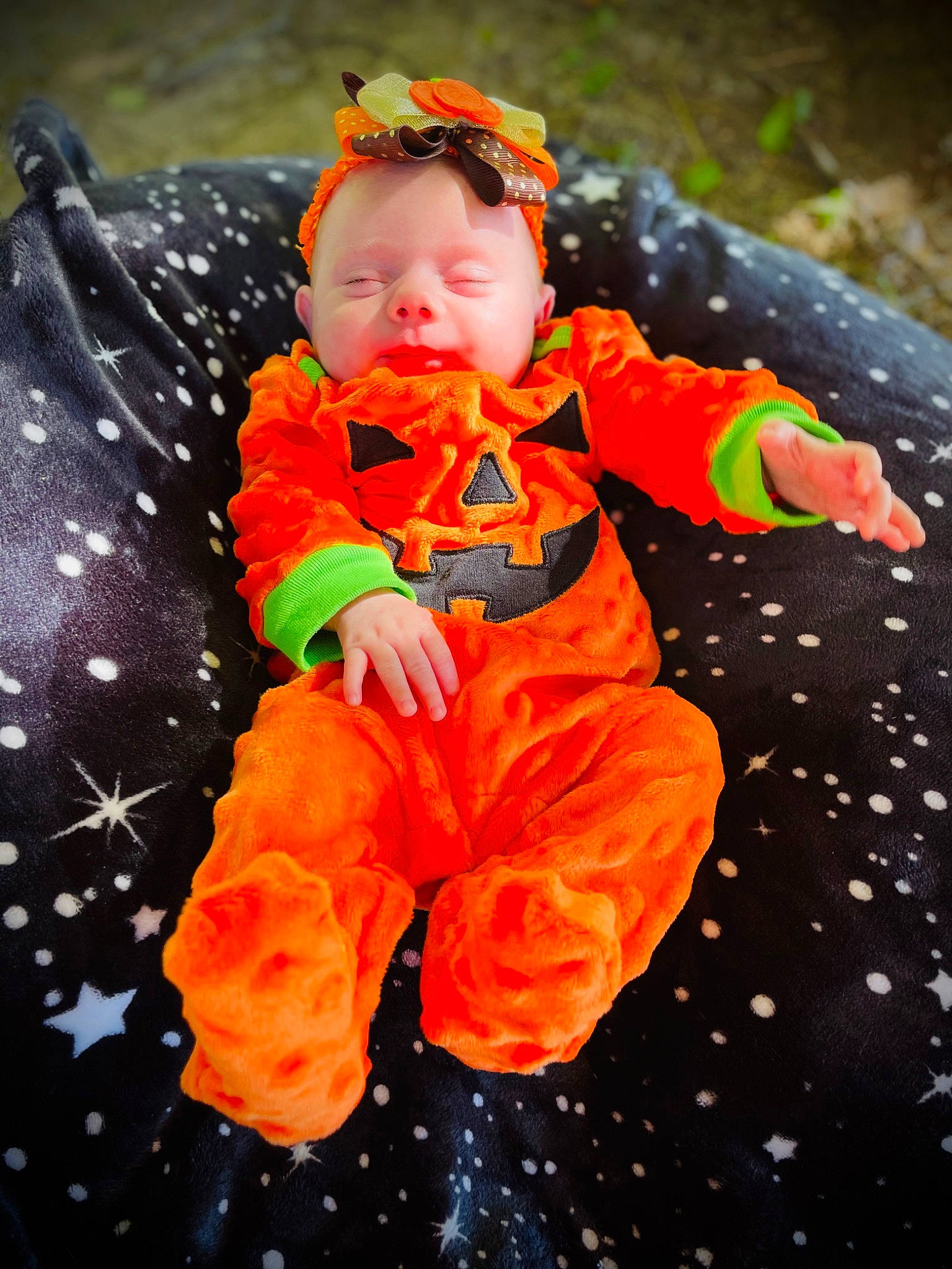 Elliana is registered to the contest to win money with this photo: baby, baby_toddler_clothing, child, face, fun, grass, happy, head, orange, people_in_nature, person, personal_protective_equipment, plant, play, pumpkin, sitting, sleeve, toddler, tree, winter